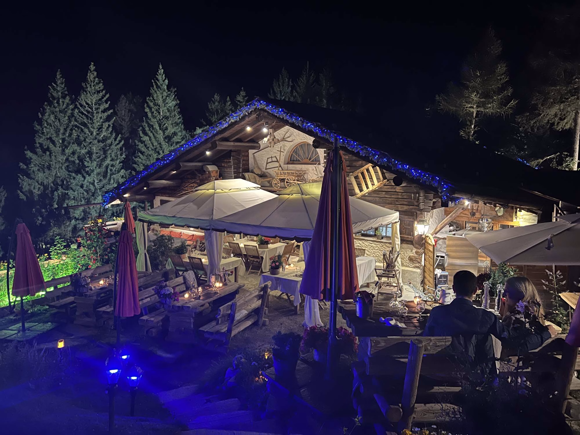 Vue panoramique du Jardin Alpin des Tables de Philippe au crépuscule, avec des tables discrètement éclairées parmi les fleurs alpines et le Mont-Blanc en arrière-plan, illustrant l'expérience gastronomique unique