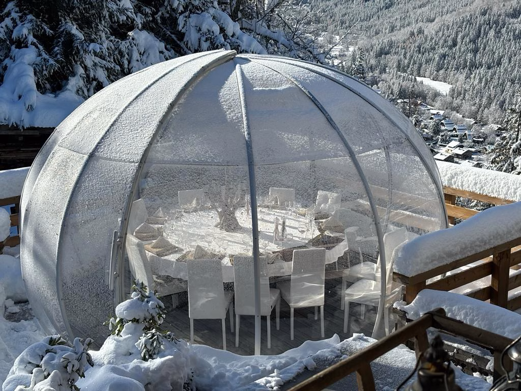 La Bulle de Philippe, dôme transparent, entourée d'un paysage hivernal enneigé, offrant une vue imprenable sur la vallée de Chamonix sous le soleil d'hiver, un cadre idéal pour une expérience gastronomique chaleureuse et exclusive.
